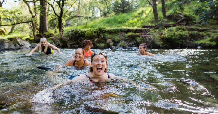 group of women wild swimming in river laughing and smiling.